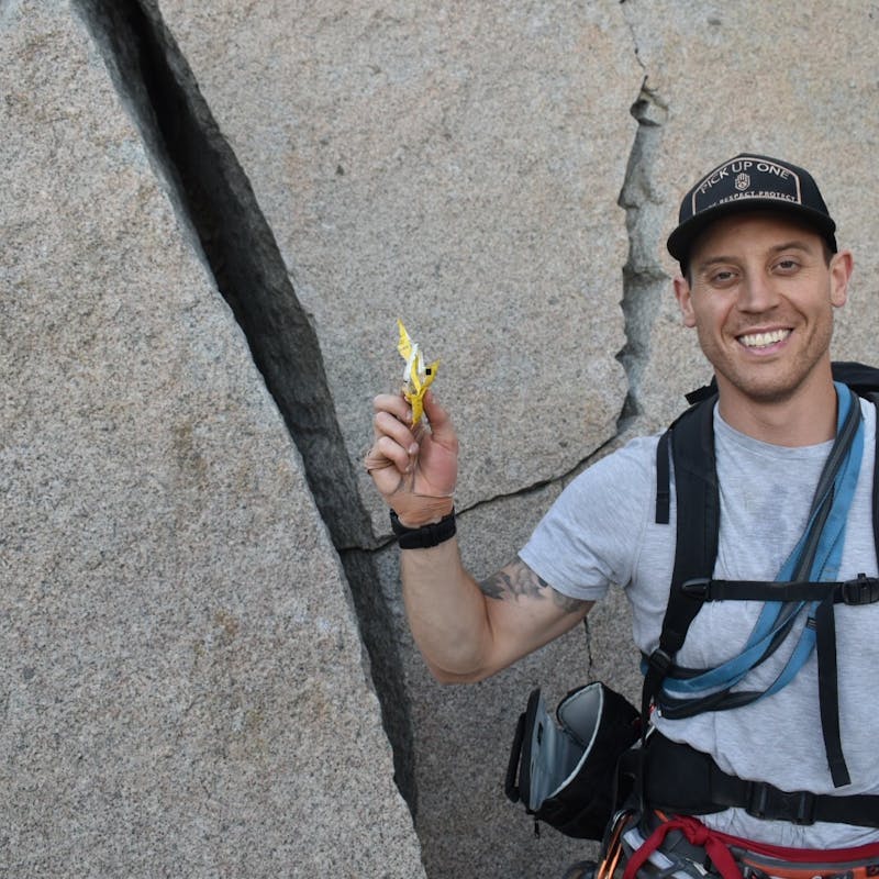 Male rock climber holding up trash in front of a boulder