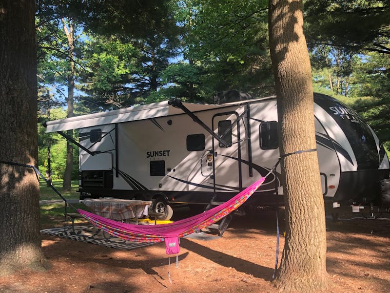 A sun dappled campsite with a hammock hung in front of an RV.