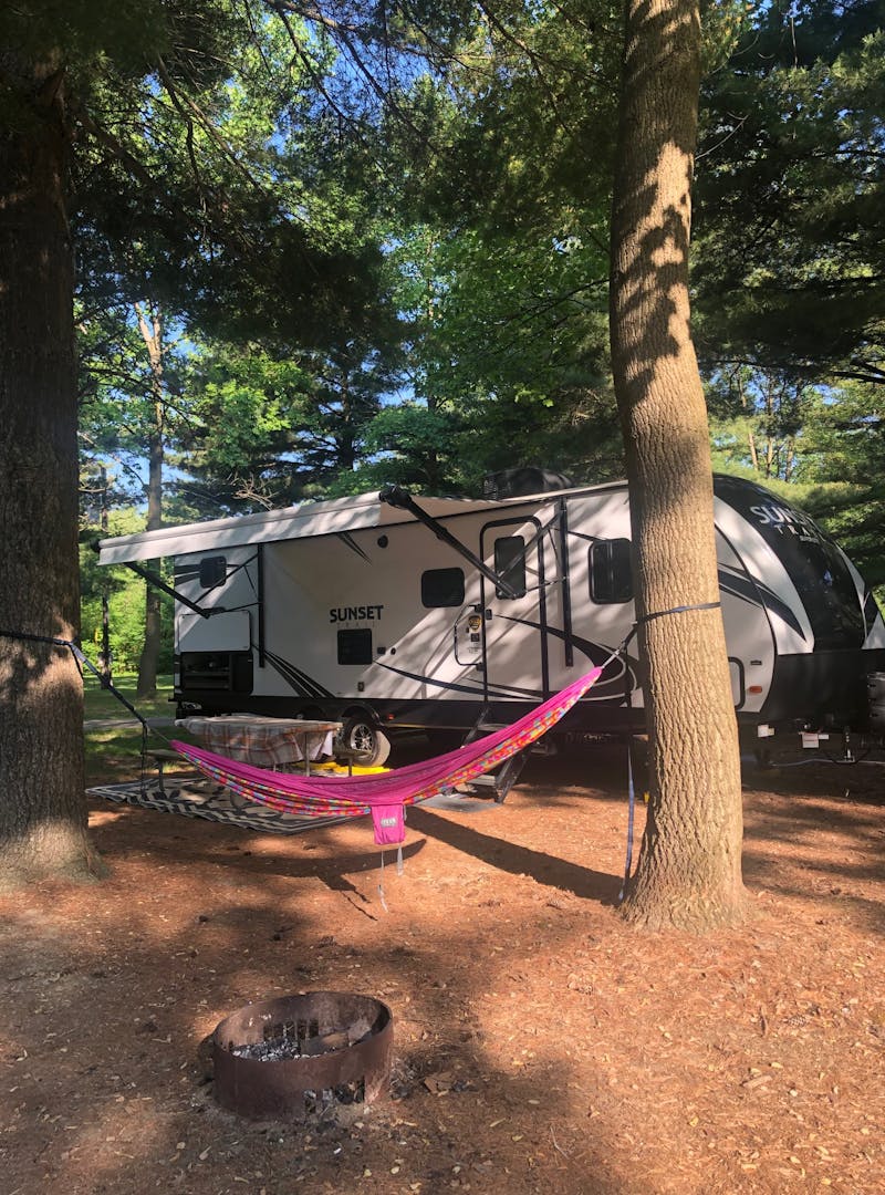 A sun dappled campsite with a hammock hung in front of an RV.