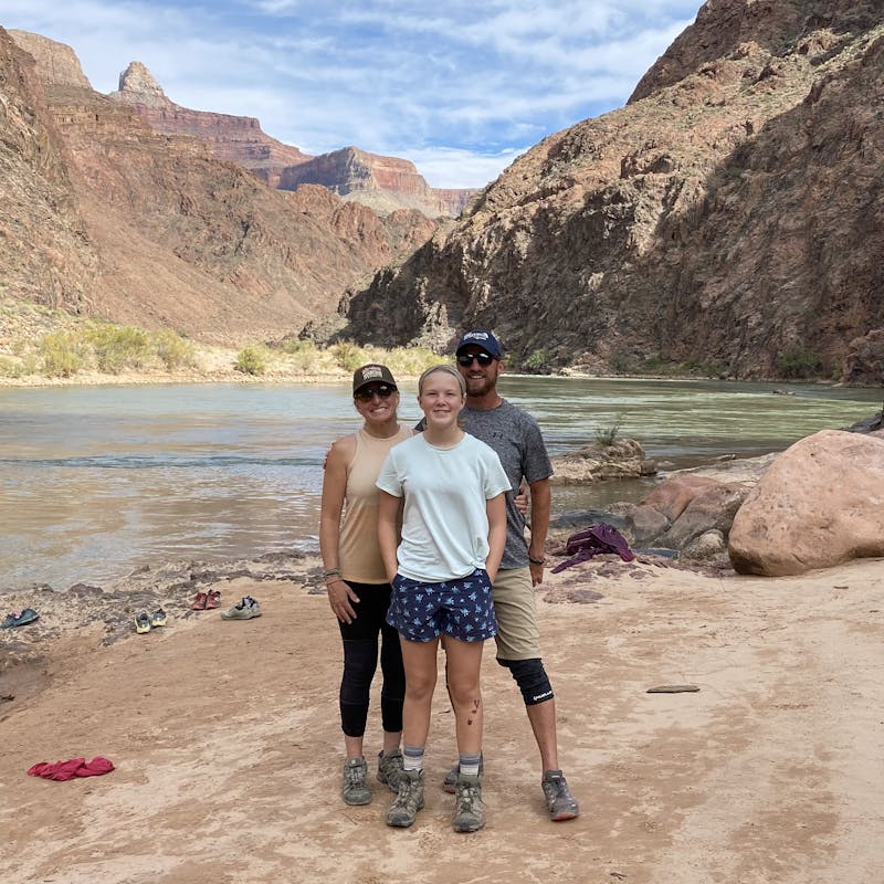 Women, man and young girl stand near a river at the bottom of a canyon