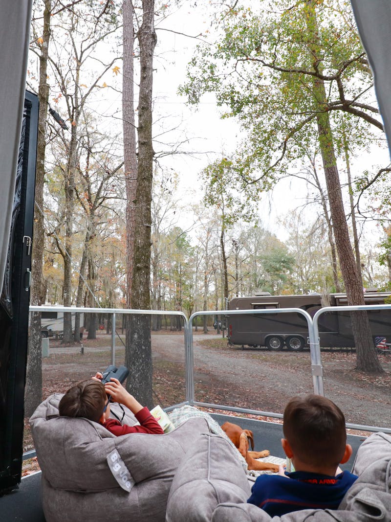 Two young boys sitting in beanbag chairs on an RV patio, looking at the trees around them.