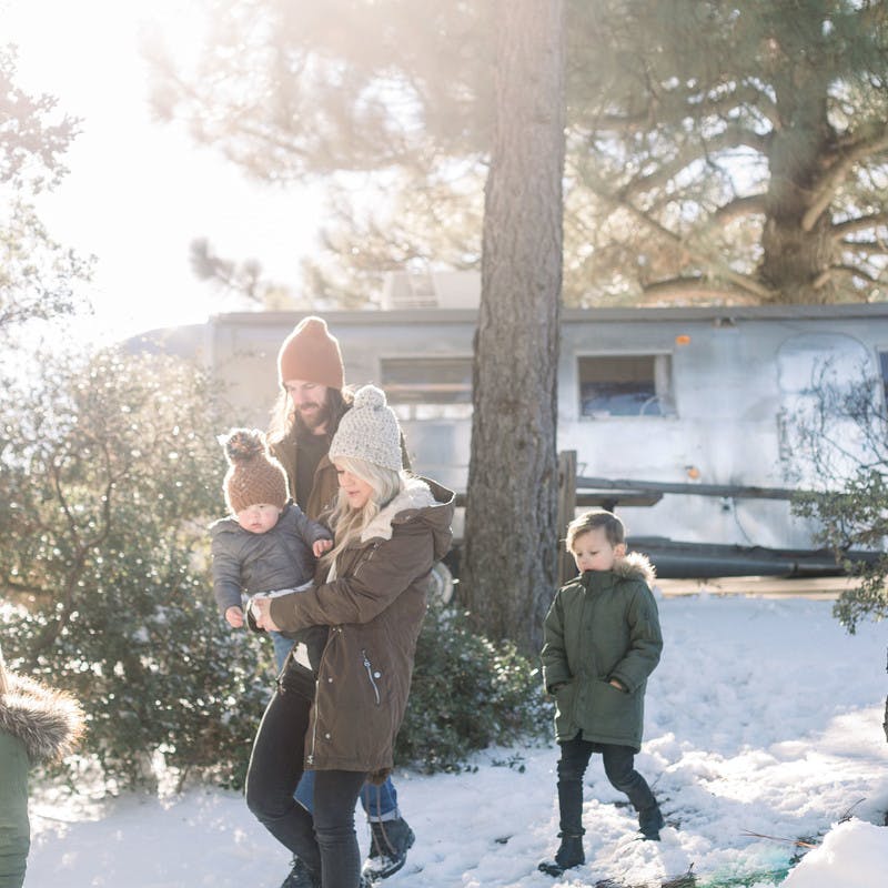 Image of Amber Thrane and her family walking in a snowy forrest, with their Airstream Travel Trailer RV in the background.