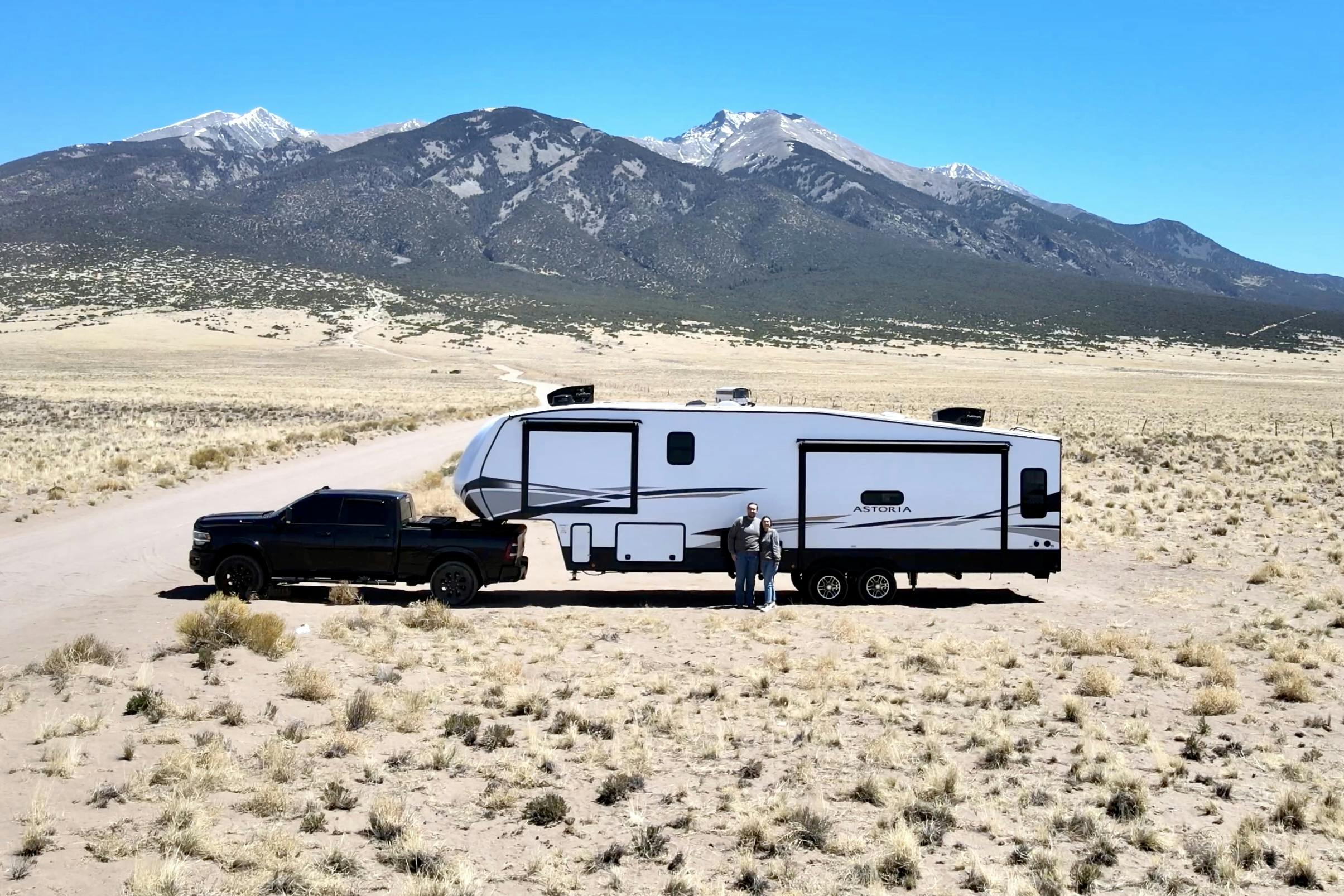 Bailey and Nicole Damberg standing in front of their Dutchmen Astoria Fifth wheel in front of mountains 