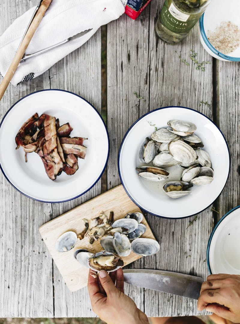 A hand separating clams from their shells with a knife.