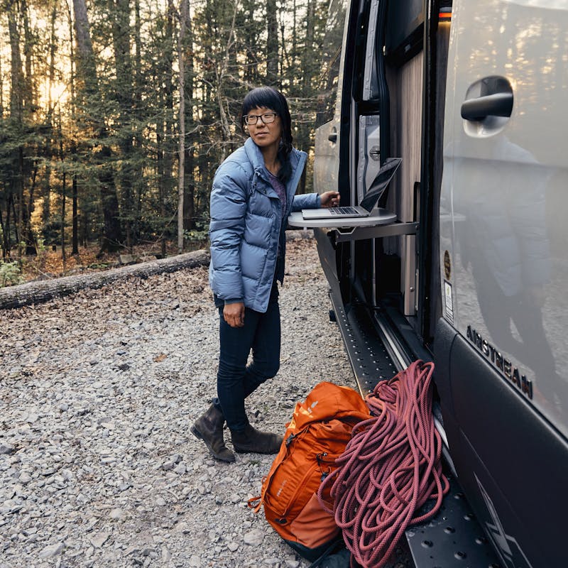 Kathy Karlo working on a laptop outside of an Airstream camper van