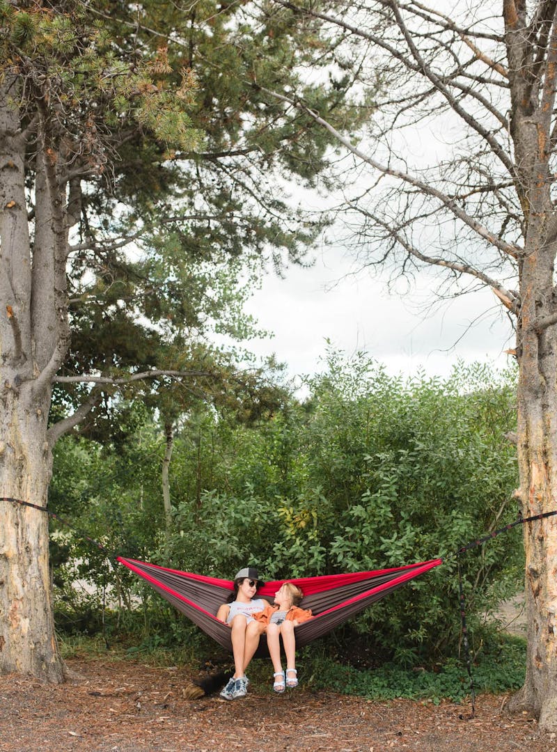 Woman and young girl sit in red hammock
