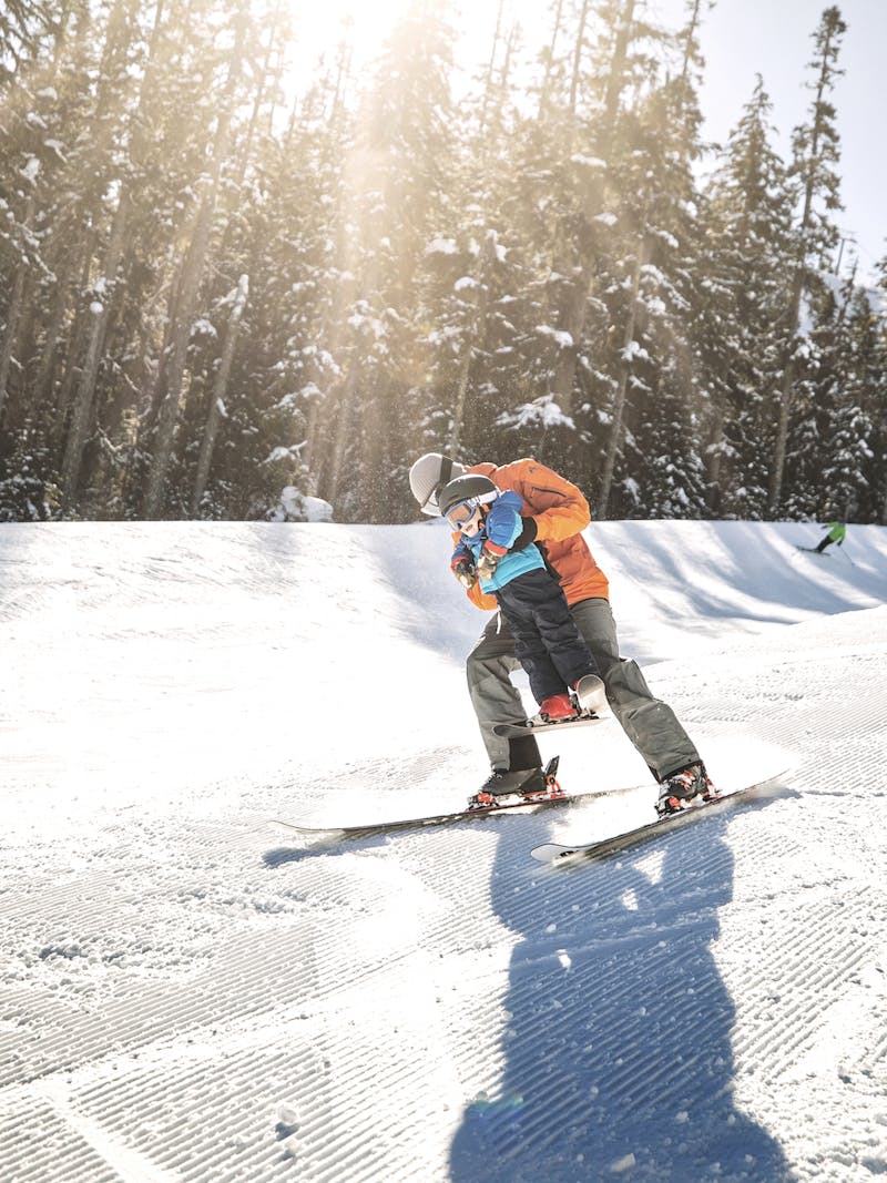 A father lifts his son as they ski down a snowy mountain in Washington.