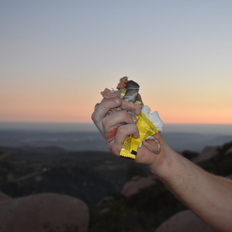 Male hand holding up fistful of trash in front of a sunset