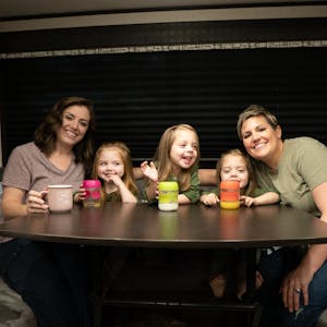 Two moms and triplet daughters around an RV table drinking milk.