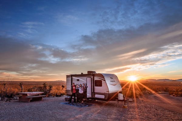 Alison and Jason Takacs pose for a photo in front of their RV with the sun setting behind them