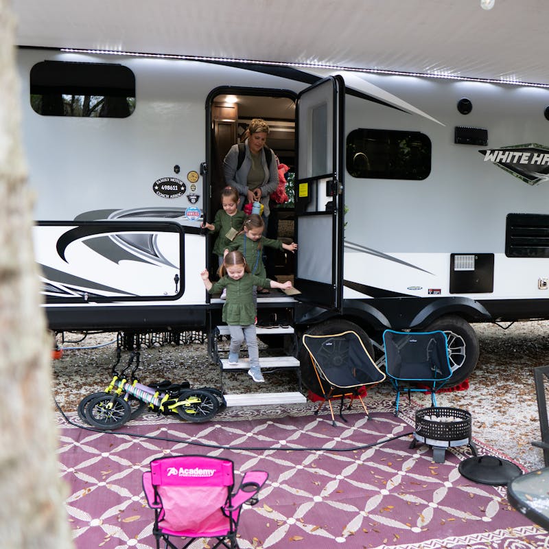 Three girls coming out of an RV with their mom behind them.