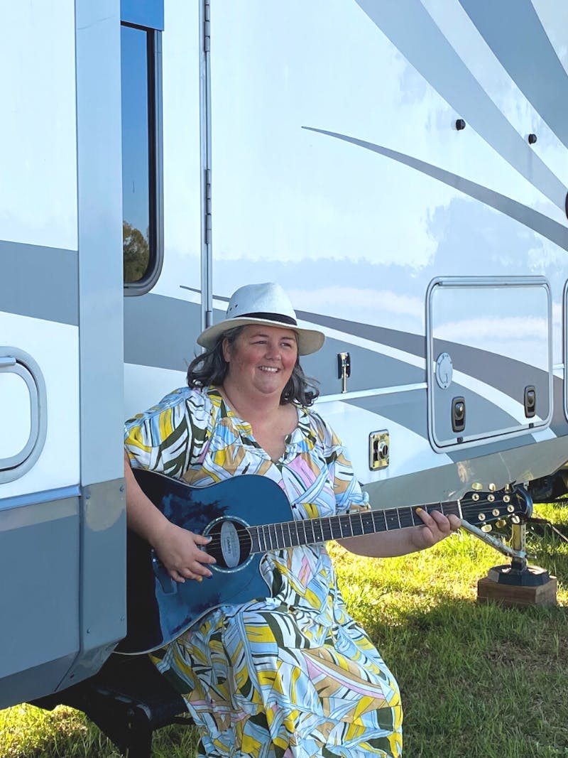 Kimberly Graham playing guitar on the staris of her RV at the Grey Fox Bluegrass Festival
