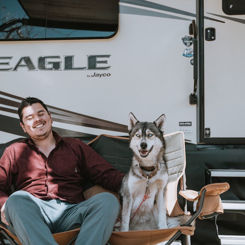 Nico sitting outside the RV with a husky in the chair next to him.
