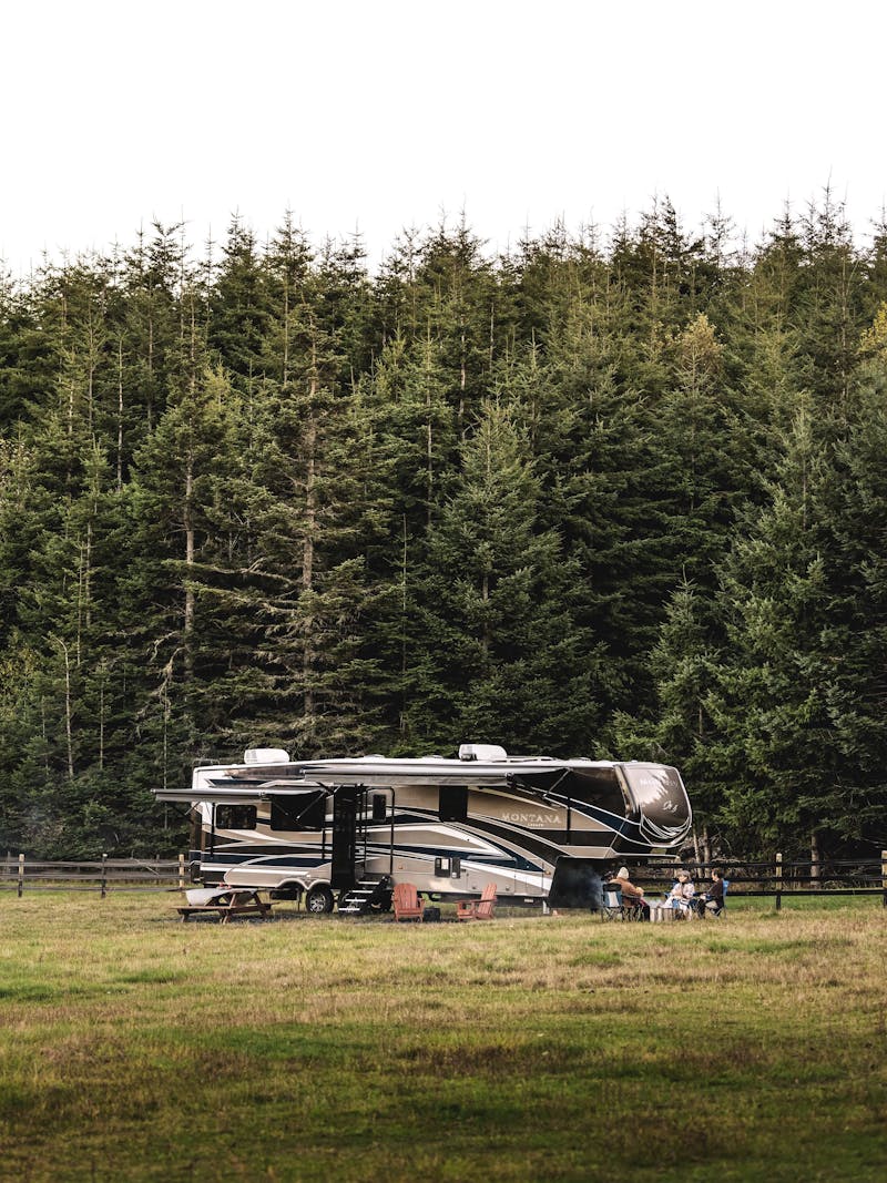 A fifth wheel RV parked in a field with a horse grazing nearby 