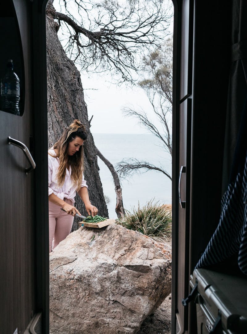Sarah Glover cutting green beans on a rock outside motorhome door.