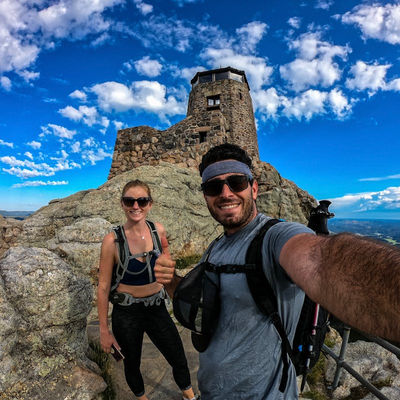 Jesse and Mel on top of a mountain with blue skies all around.