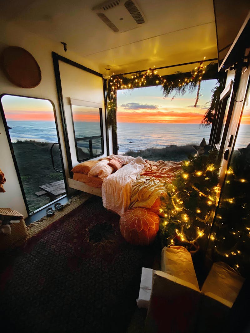 The view out an RV decorated with lights and pine for Christmas, with the window facing the sunset over a beach.