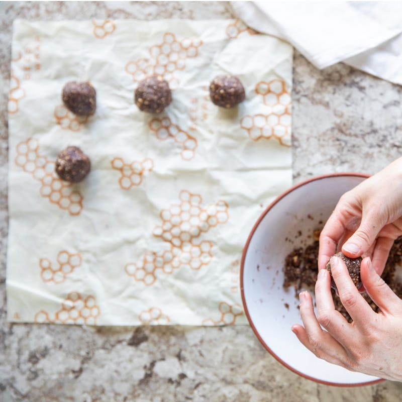 Hands rolling chia seed dough into small balls and placing them on bees' wax paper.