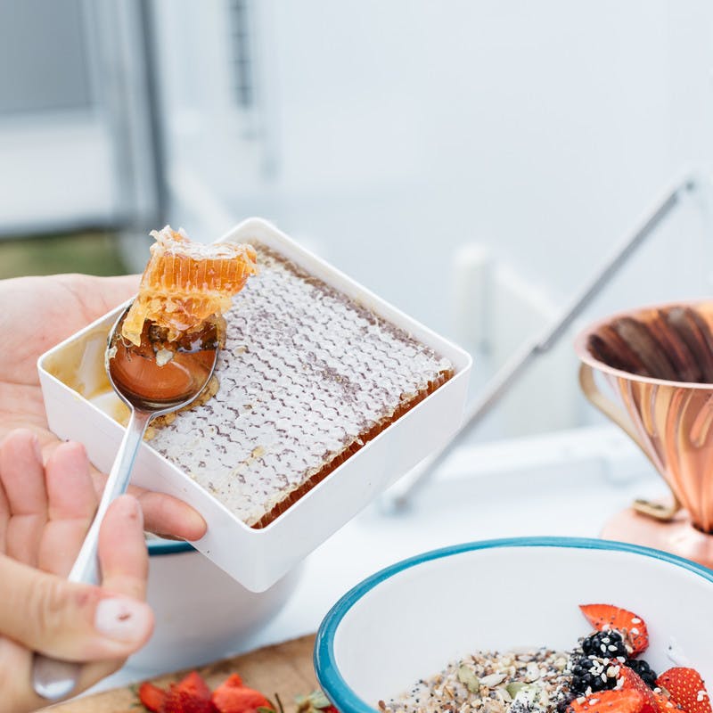 A hand scoops a chunk of fresh honeycomb out of a container to add it to the overnight oats.