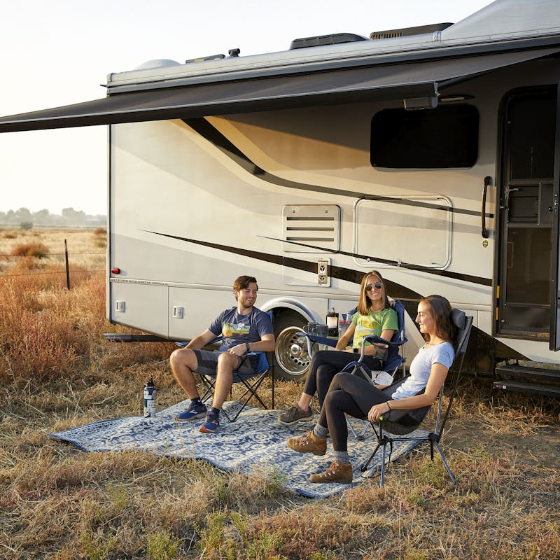 Group of young adults sitting on camp chairs outside of a Class C RV