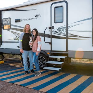 A young couple and their small doc stand outside their Heartland Open Range RV posing for a picture.