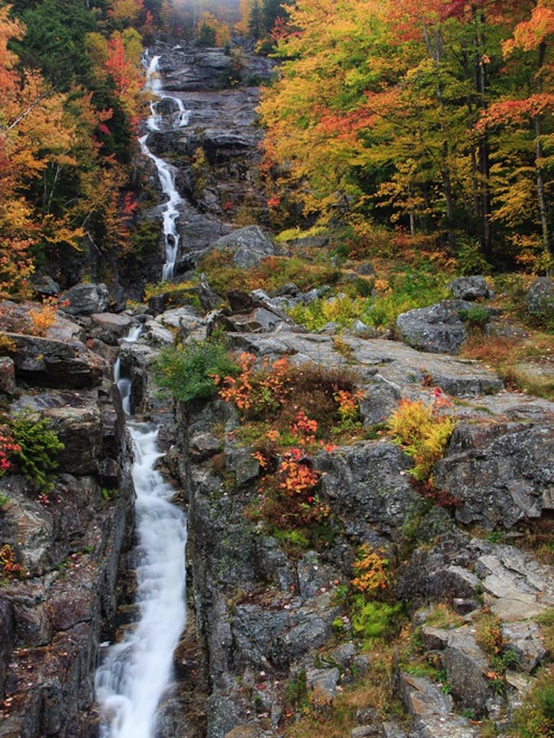 Waterfall surrounded by colorful fall trees and dark rocks