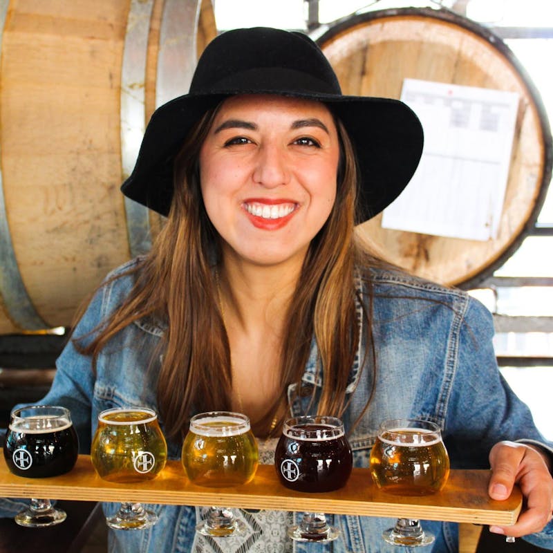 Rachael Lyons smiles holding up a beer flight.