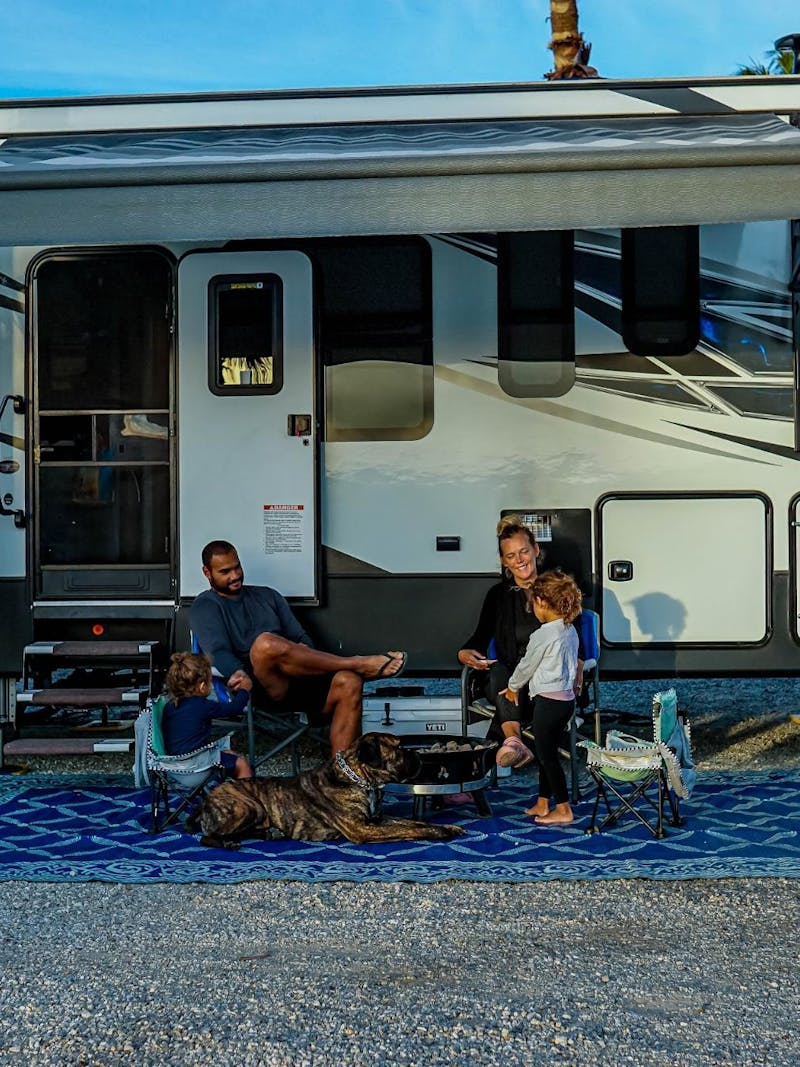 Samantha and Blake sit under the awning of their Dutchmen Voltage with two children.