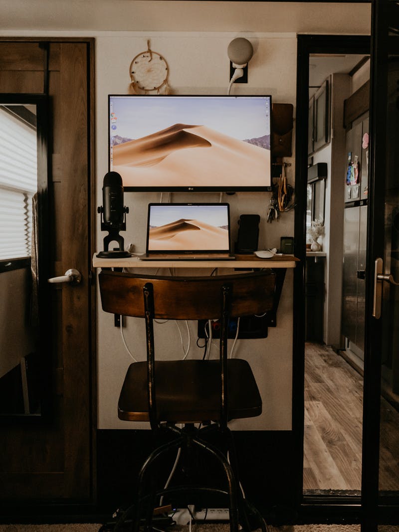 A laptop and a bigger screen set up at a narrow, but efficient work desk inside an RV bedroom. 