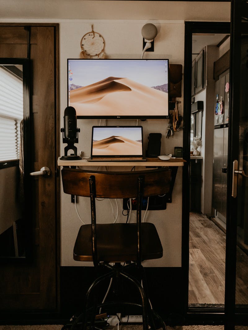 A laptop and a bigger screen set up at a narrow, but efficient work desk inside an RV bedroom.