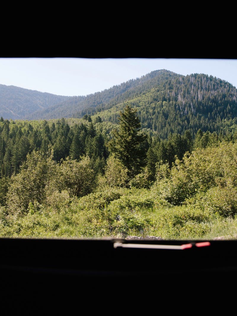 A view from inside an RV looking out the window to see mountains filled with lush, green trees.