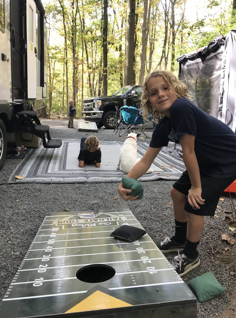 A young boy playing cornhole at a camp site.