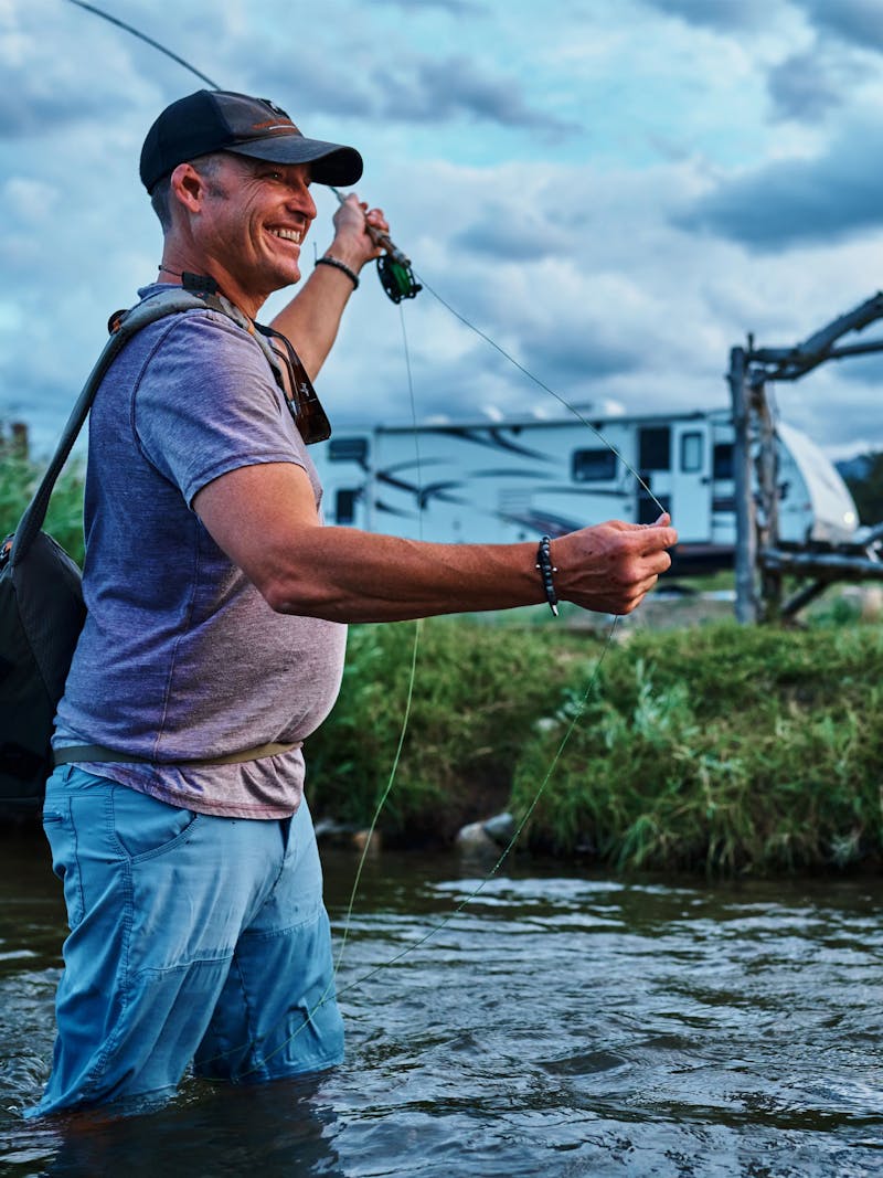 CHRIS HEUBLEIN fishing in a river next to his Keystone Passport RV