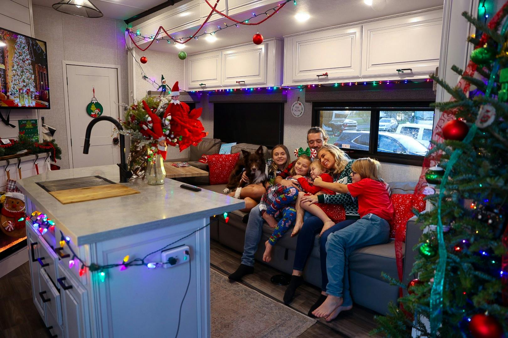 The Cassie and Joshua Bailey family sitting on a couch in a living room with Christmas decorations inside their Highland Ridge Open Range fifth wheel.