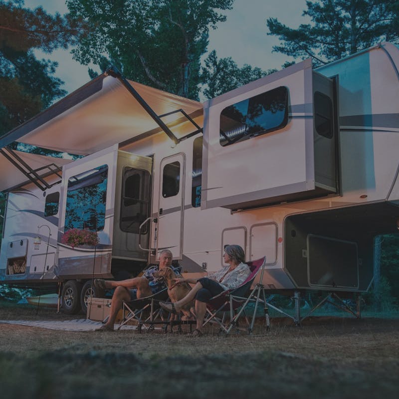 Highland Ridge Fifth wheel with a couple sitting in front of it with camp chairs