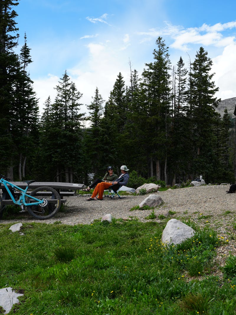 Dustin and Sarah Bauer sitting at a picnic table at a campsite with their Tiffin Wayfarer Class C Motorhome in Medicine Bow Routt National Forest