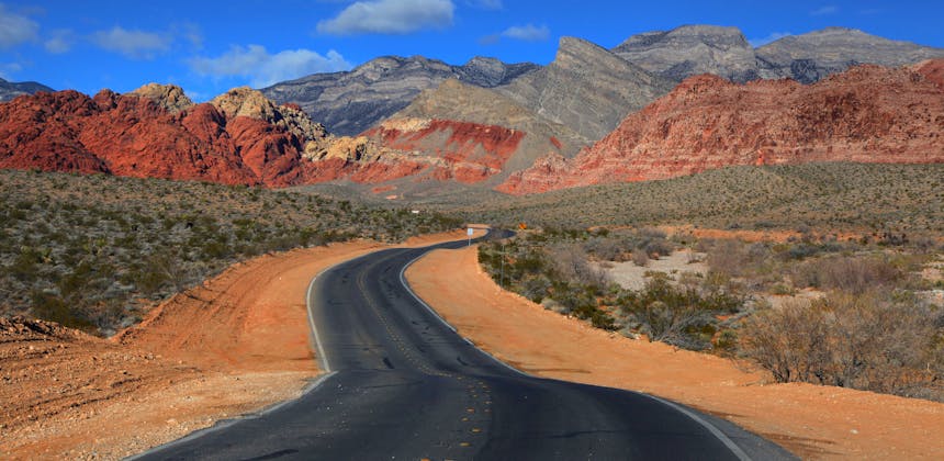 A road running through a desert landscape up to red rocky mountains.