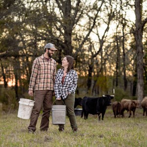 Todd & Marcia Schabel smile at each other holding buckets of crops on a farm.