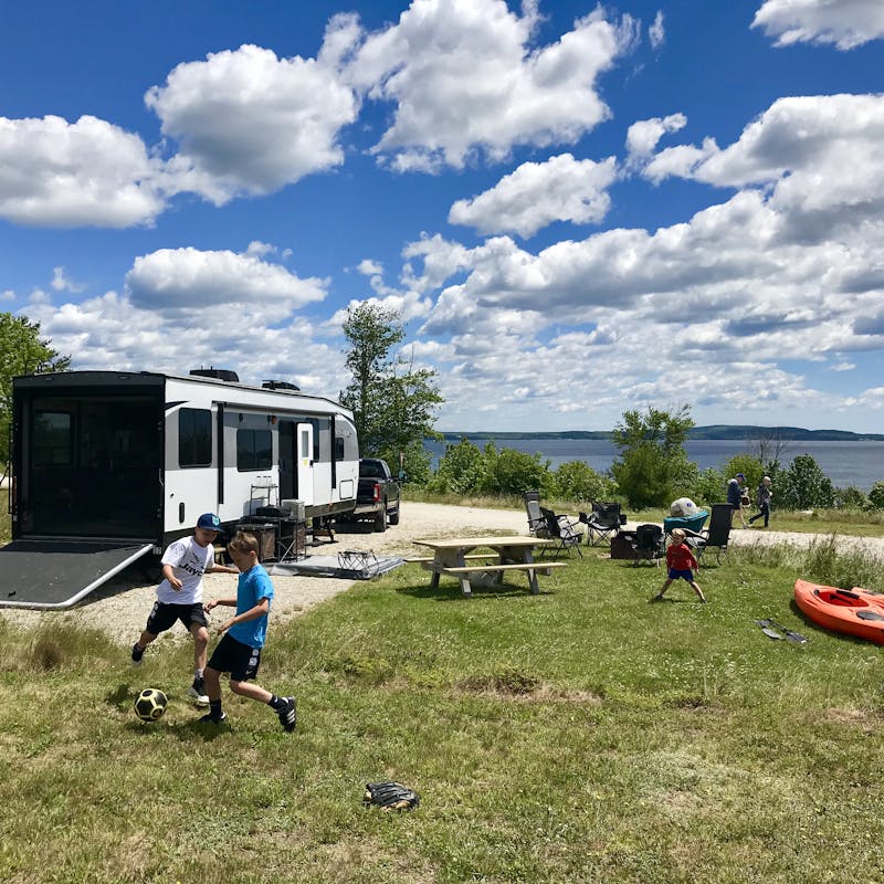 Boys play in the grass on a beautiful, sunny day with the Toy Hauler parked at the edge of a lake.