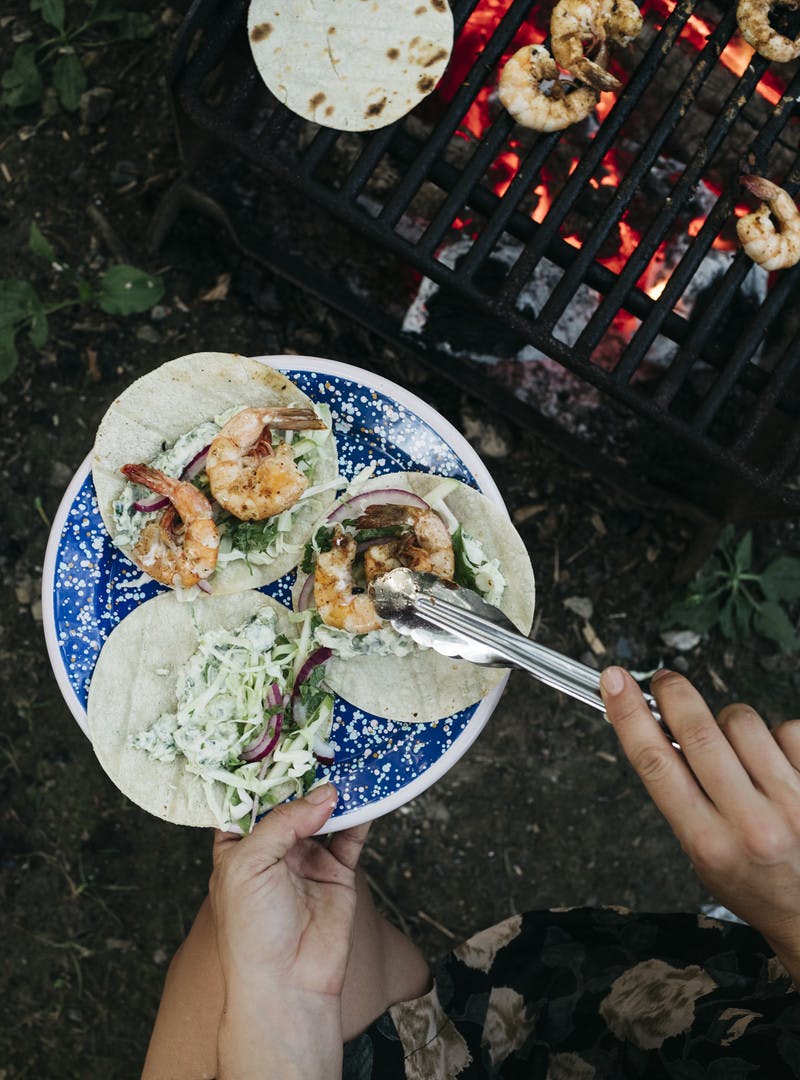 Assembling three shrimp tacos on a plate by taking shrimp off the grill.