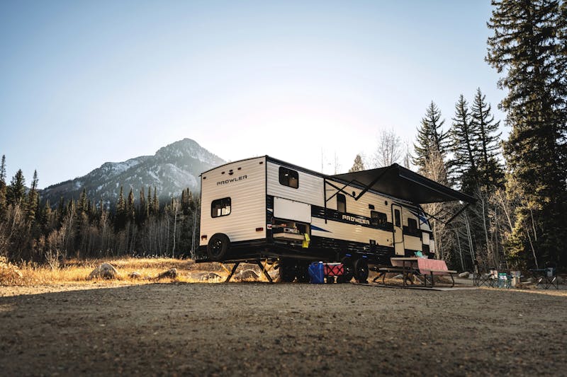 A Heartland Prowler camping in the forrest near mountains