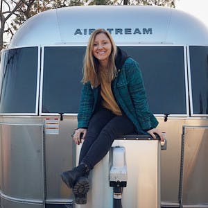 A photo of Stacey Powers sitting on her classic Airstream travel trailer RV.
