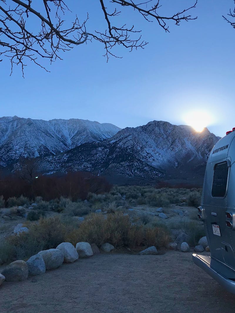 Dr. Na's Airstream parked at a campsite with snow capped mountains in the distance.