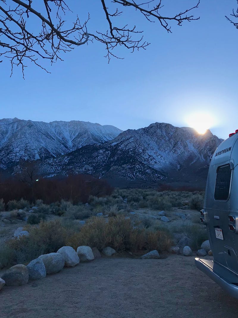 Dr. Na's Airstream parked at a campsite with snow capped mountains in the distance. 