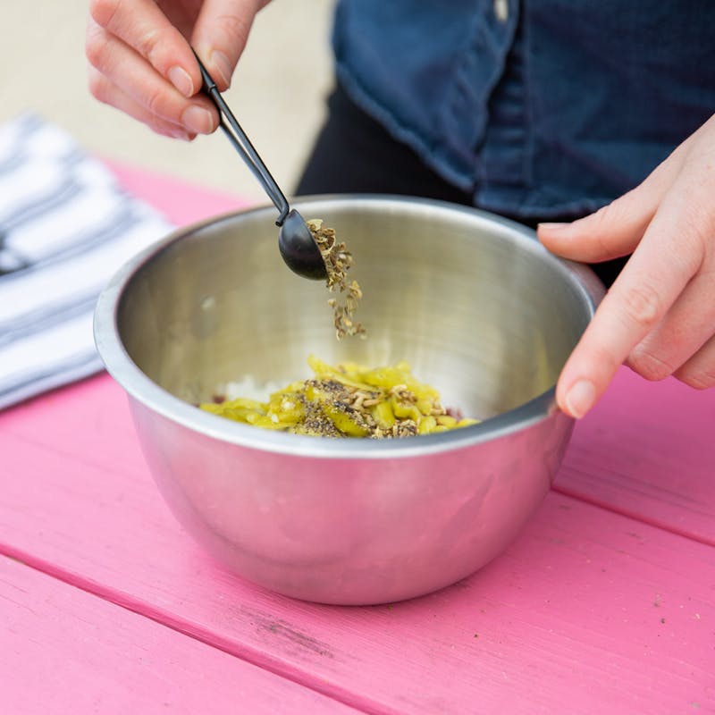 Mixing peppers, capers and olives together in a metal bowl.