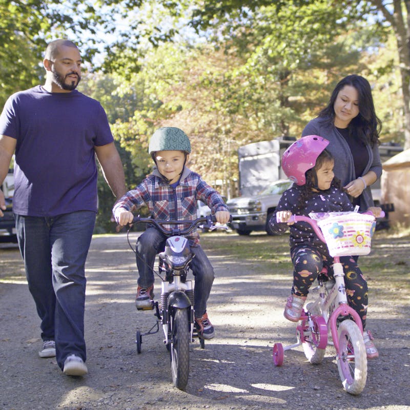 Luis and Sandra walking alongside their kids riding bikes through an RV campground.
