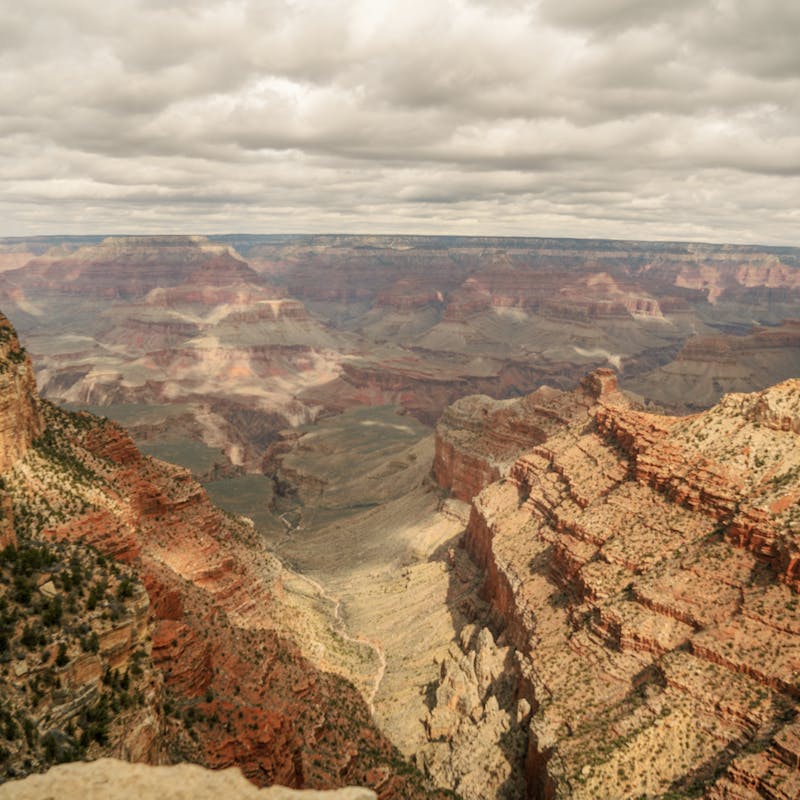View looking out over the South Rim of Grand Canyon with lots of layered red rock and cloudy skies