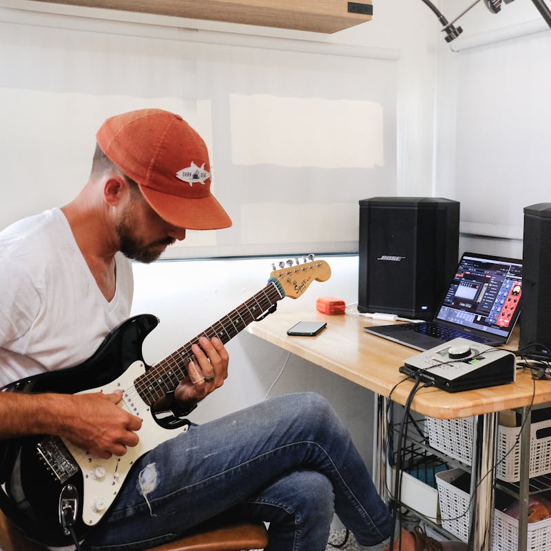 Amick Cutler plays guitar by a desk in an RV.