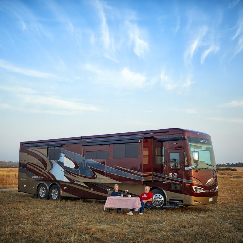 Class A RV featuring Airxcel products parked in a field with a couple sitting out front