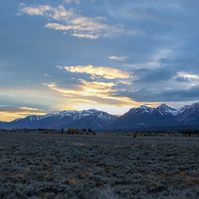 Snowy peaked mountains with grassy field and sunset sky
